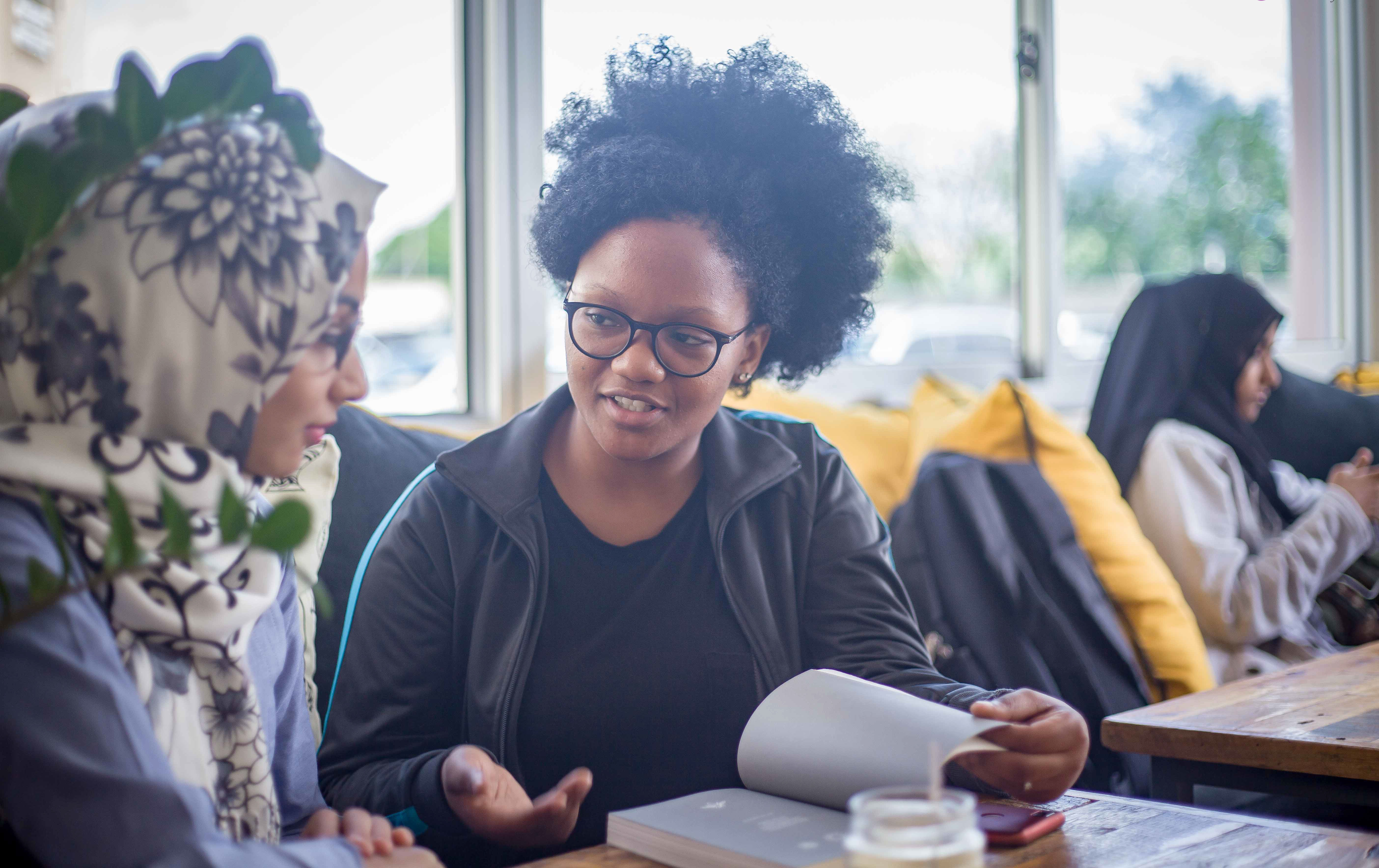 Two women in a community workshop, one reading from a notebook