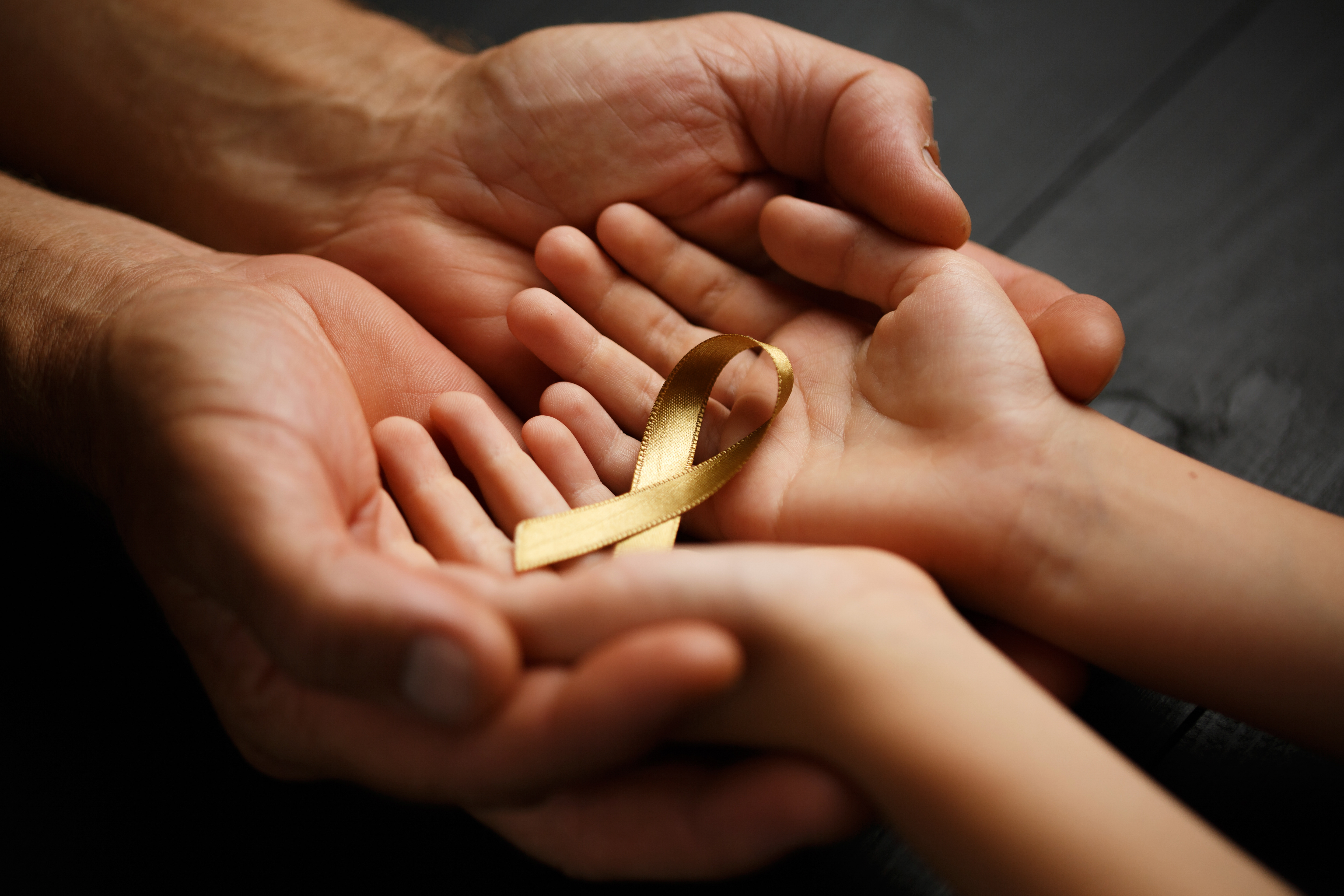 Adult and child hands cradling a golden ribbon